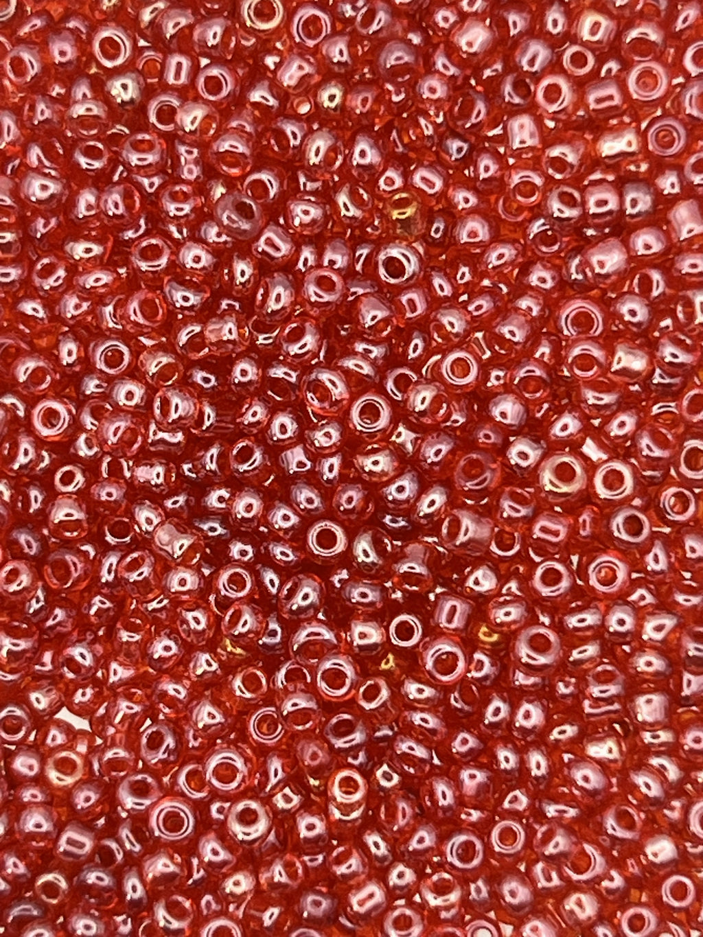 Close-up of 12/0 transparent lustered red glass seed beads with a high-shine finish.