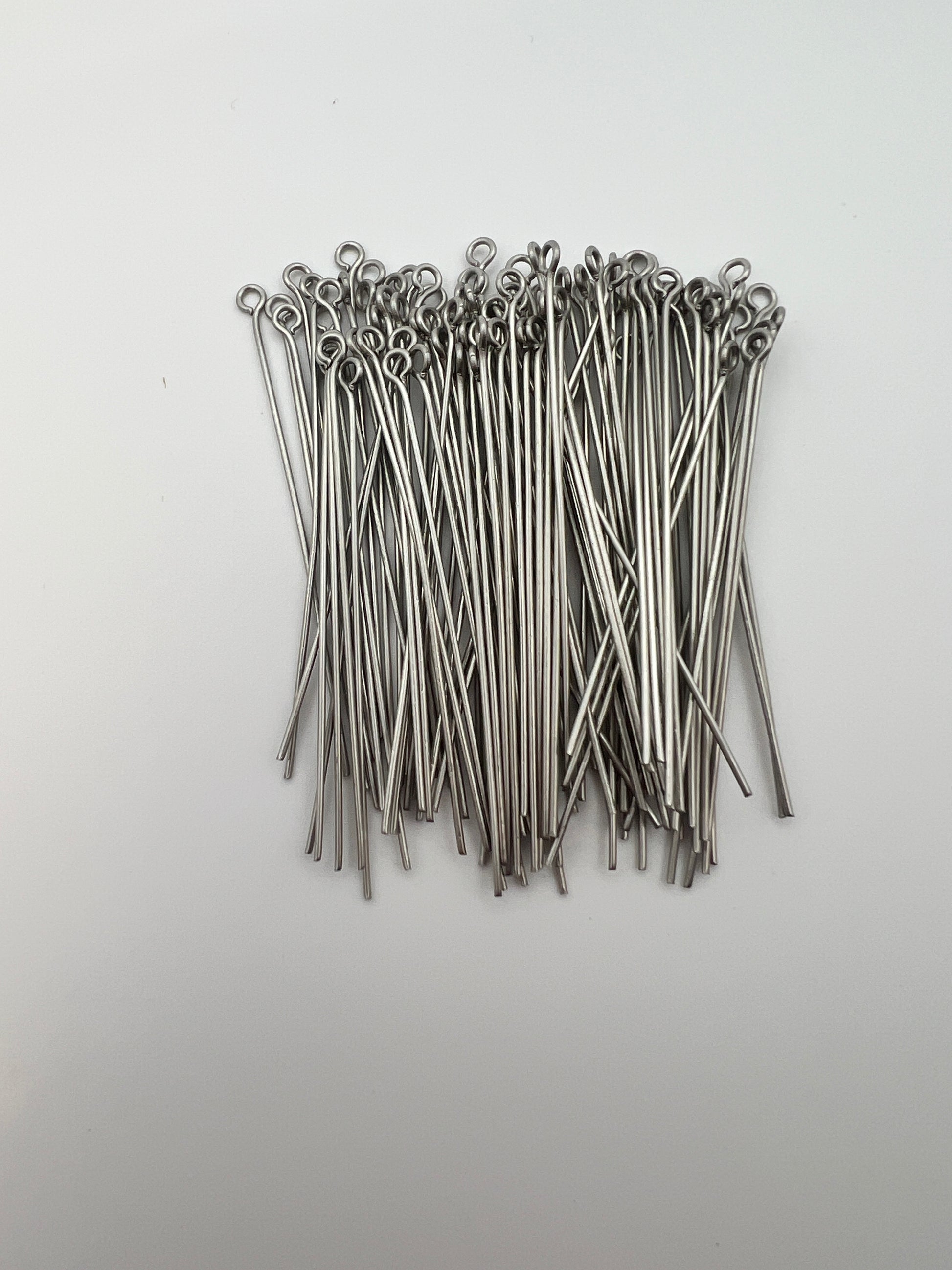 A bulk bag of 50mm 304 stainless steel eye pins for jewelry making on a white background.