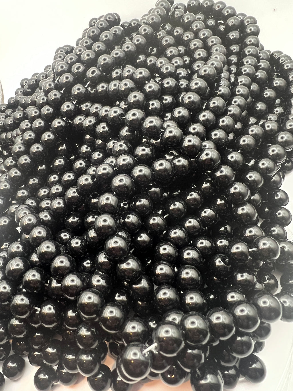 A pile of lustrous 10mm black glass pearl beads with a glossy finish.