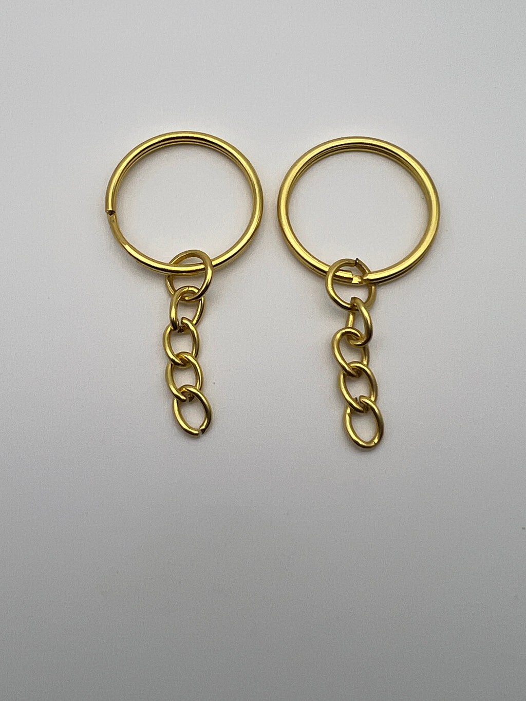 Two golden split key rings with attached curb chains on a plain white background.