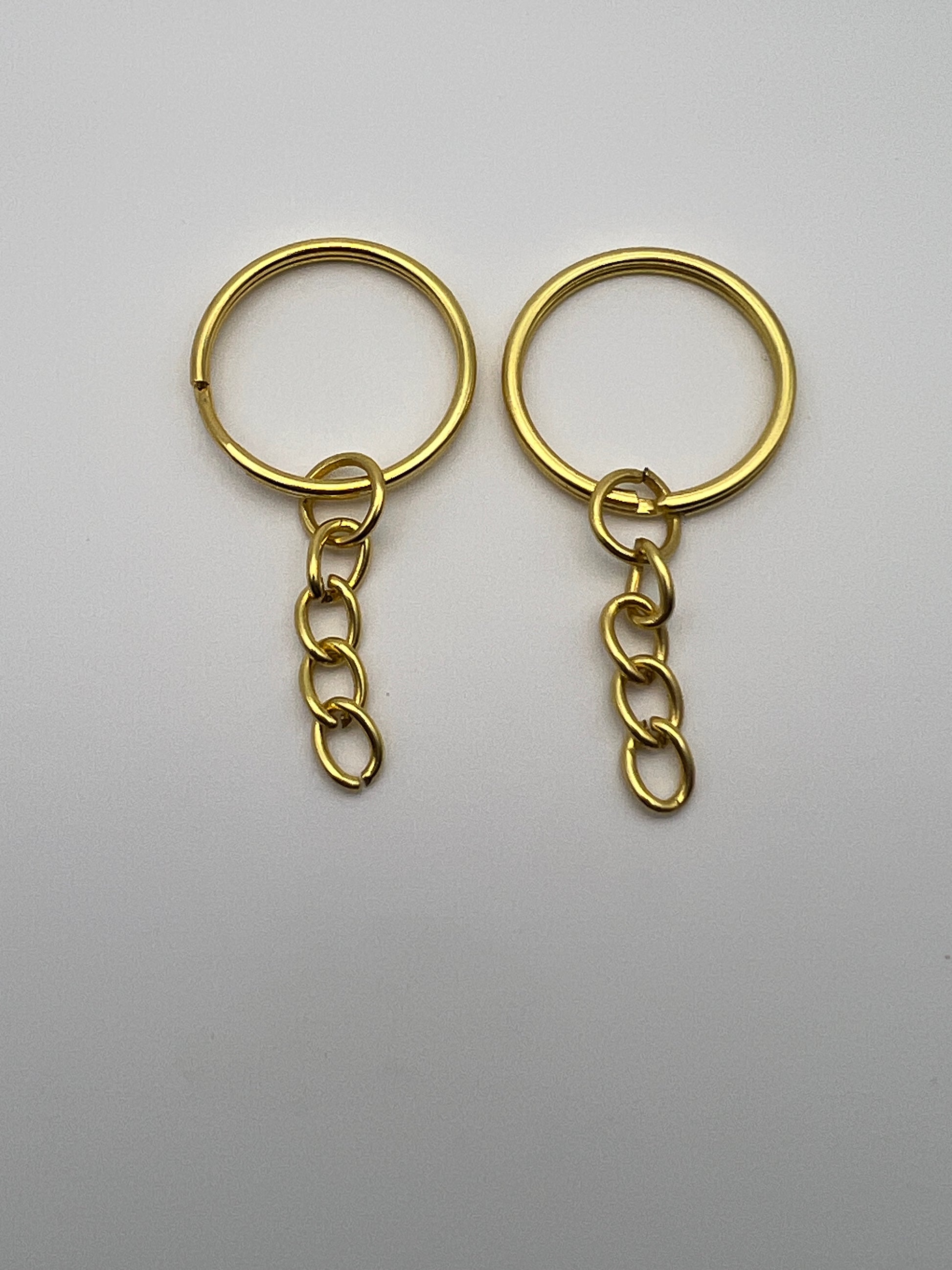 Two golden split key rings with attached curb chains on a plain white background.
