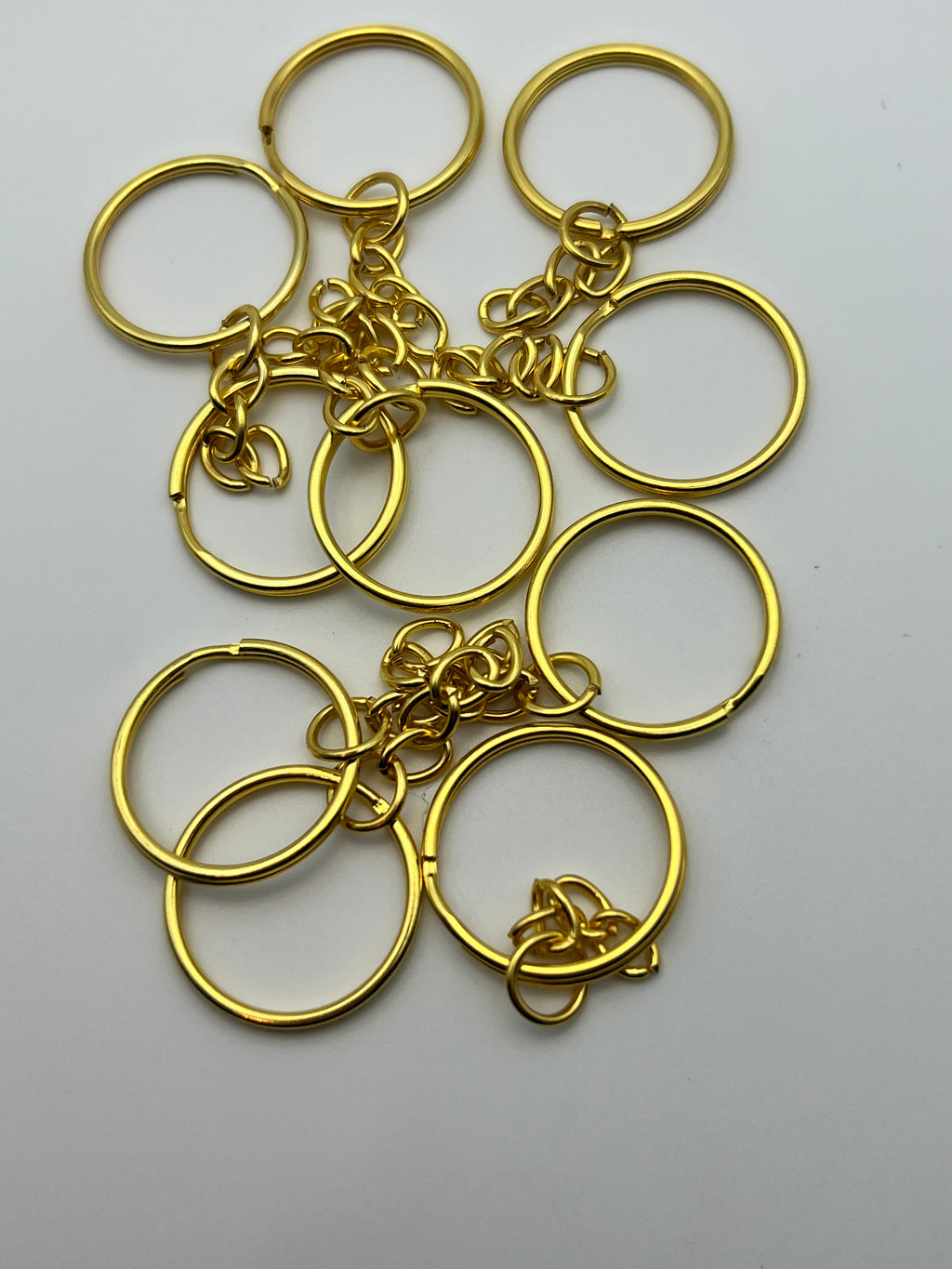 Ten golden split key rings with attached curb chains scattered on a white background.