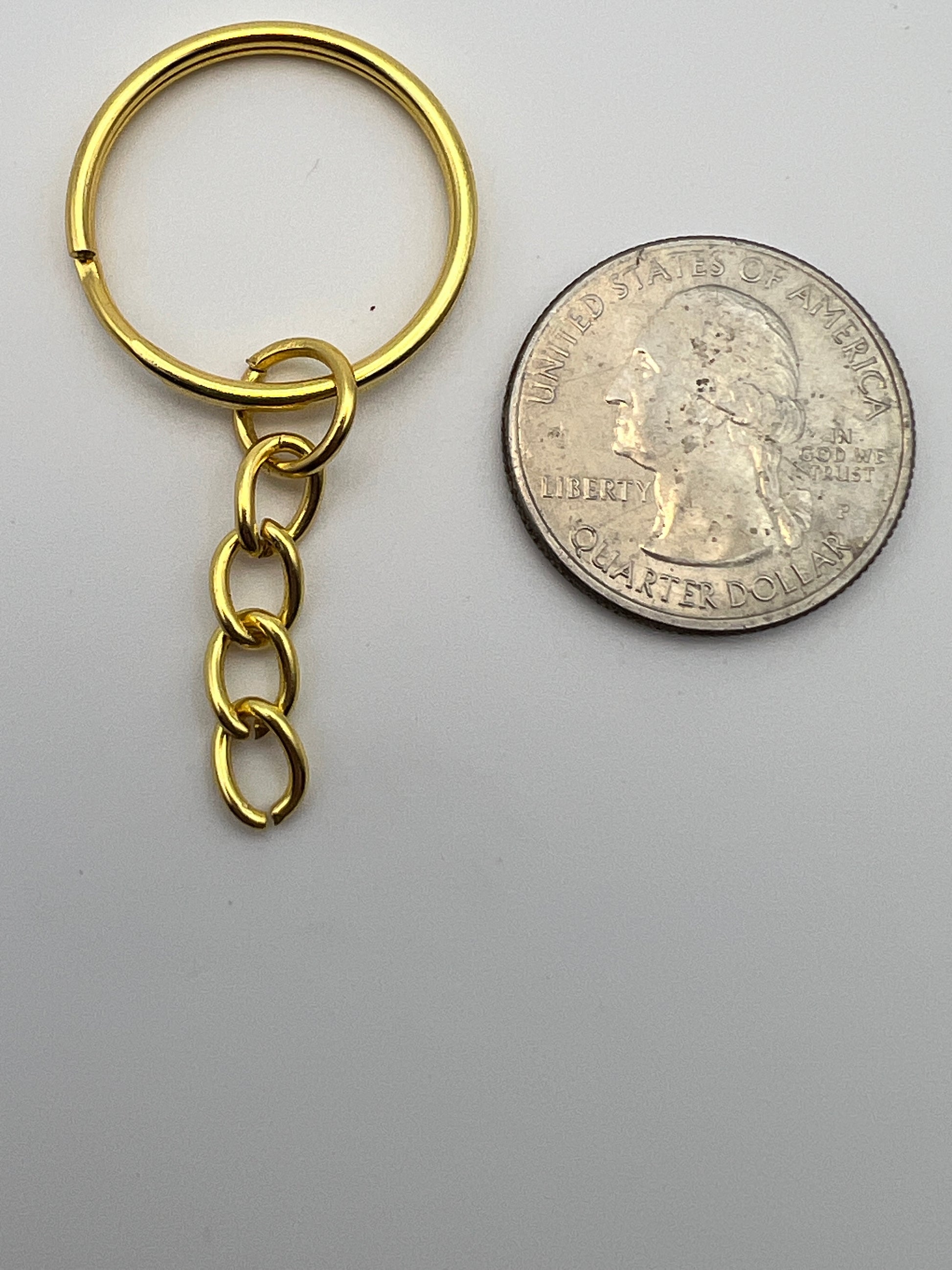 Golden split key ring with a four-link curb chain next to a US quarter for size comparison.