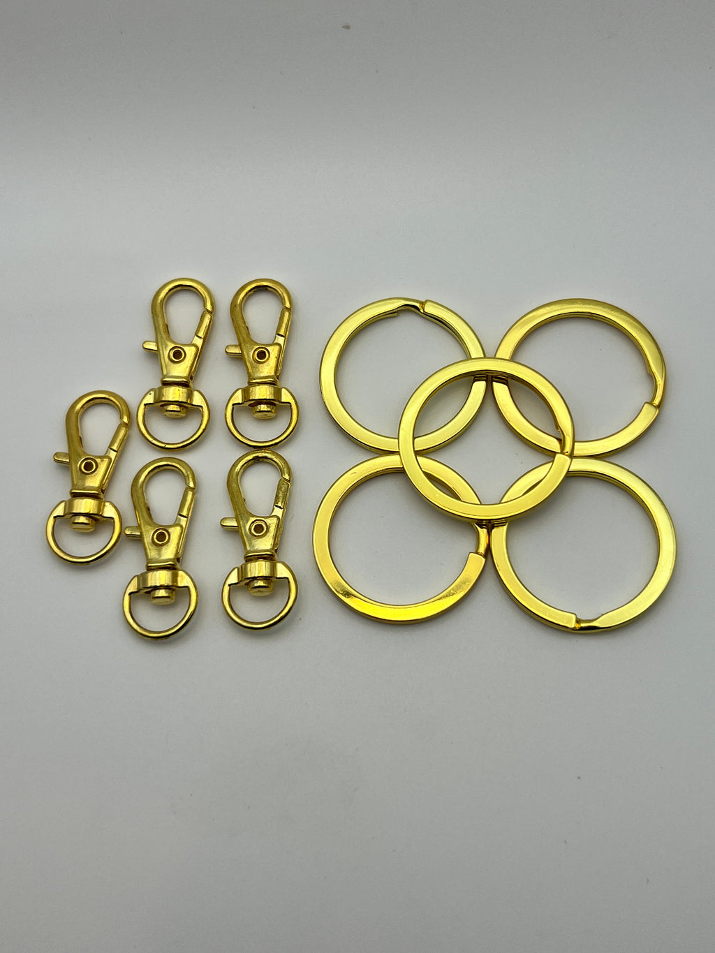 Five golden split key rings and five matching swivel lobster clasps on a white background.