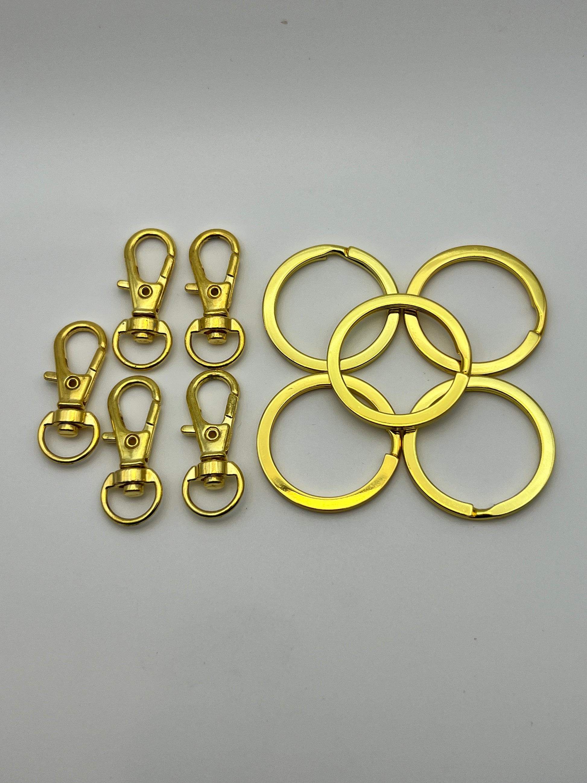 Five golden split key rings and five matching swivel lobster clasps on a white background.