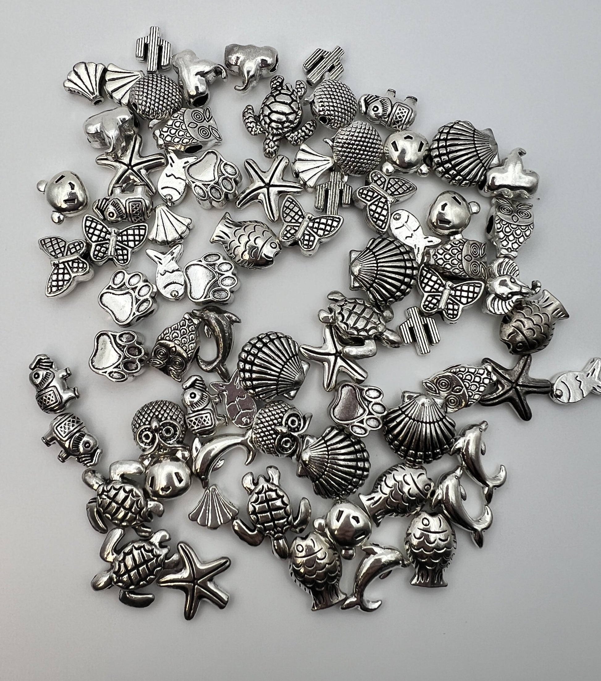 Assorted silver Tibetan style beads in 15 designs including owls, turtles, fish, and shells.
