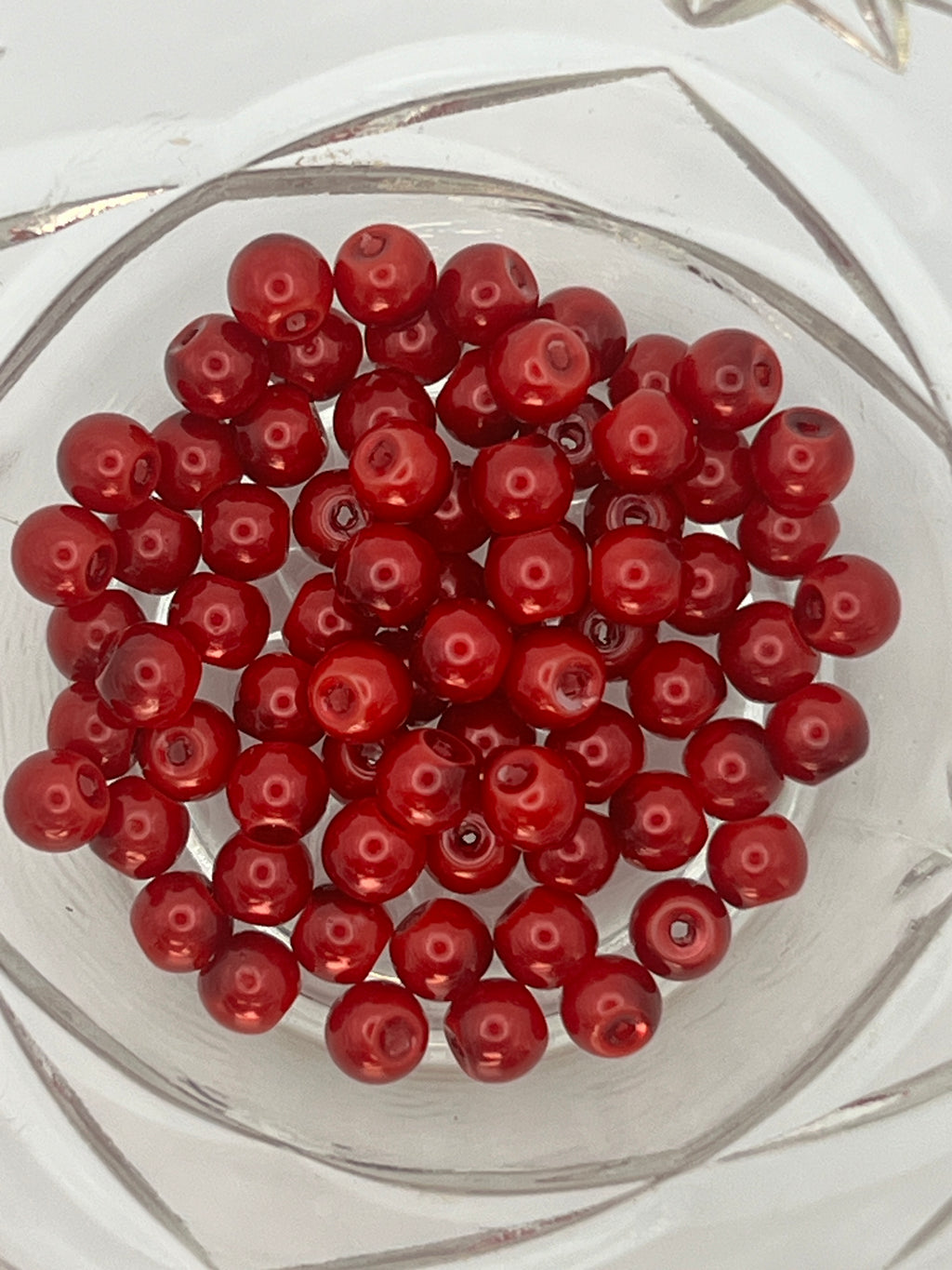 A top-down view of 75 crimson 6mm glass pearl beads gathered in a clear glass bowl.