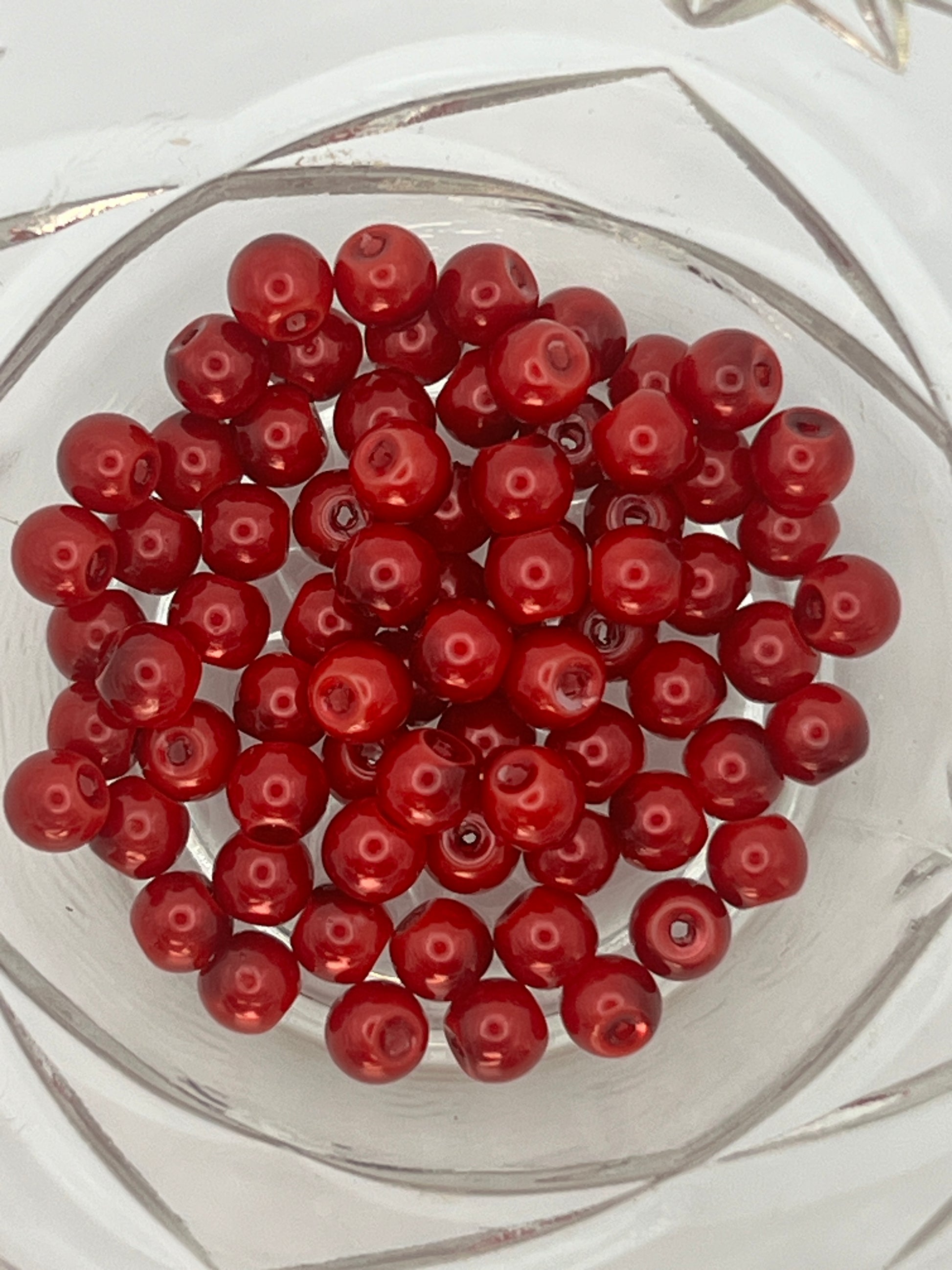 A top-down view of 75 crimson 6mm glass pearl beads gathered in a clear glass bowl.