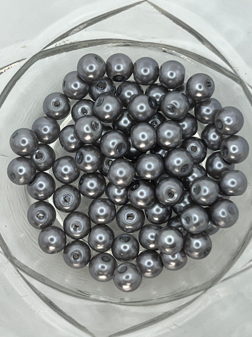 A collection of 6mm slate gray glass pearl beads with a metallic luster in a clear glass bowl.