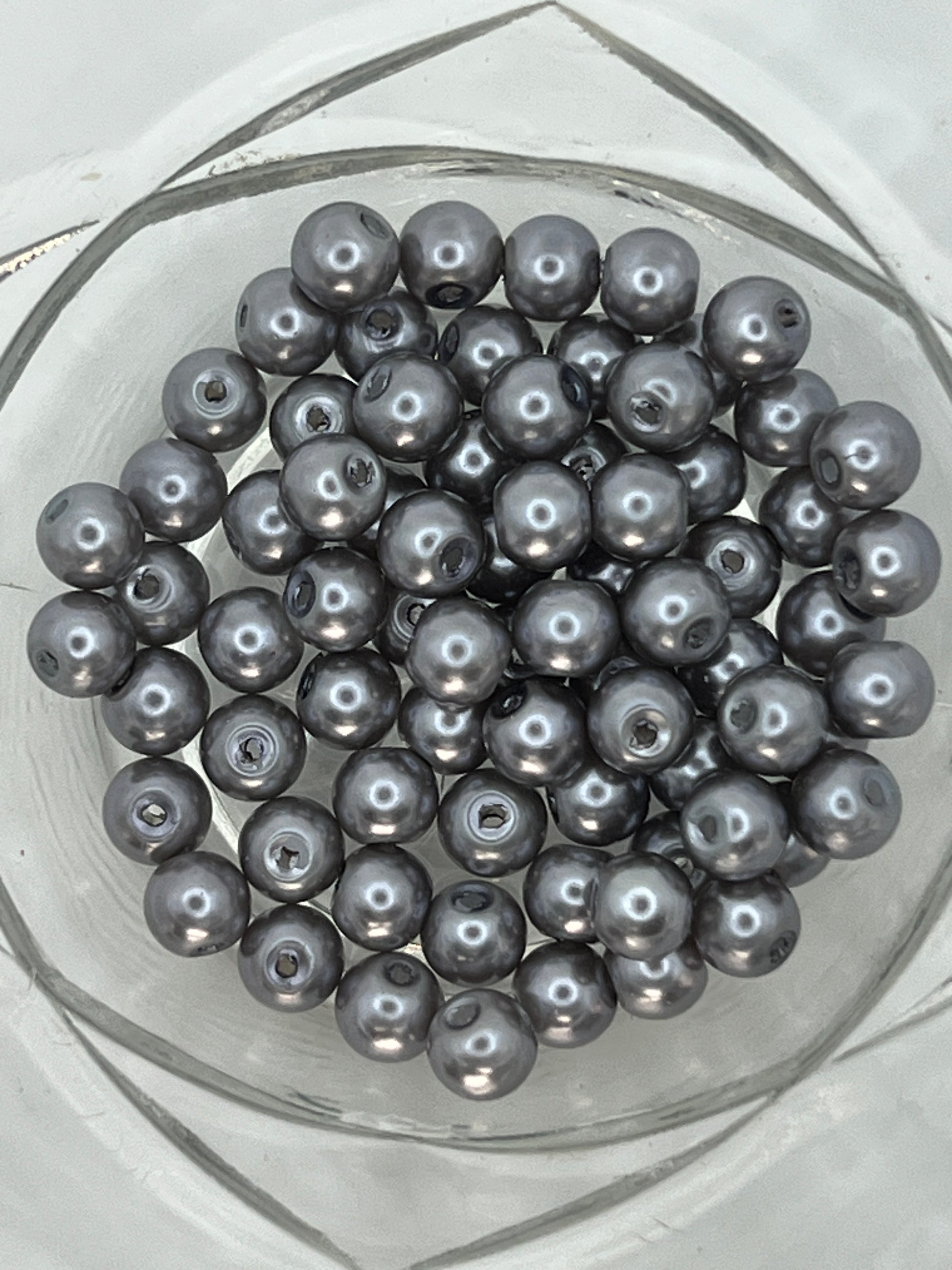 A collection of 6mm slate gray glass pearl beads with a metallic luster in a clear glass bowl.