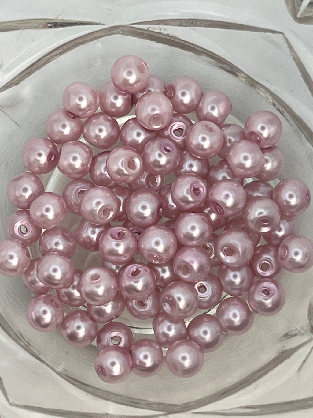 A cluster of 6mm flamingo pink glass pearl beads with a lustrous finish in a clear glass bowl.