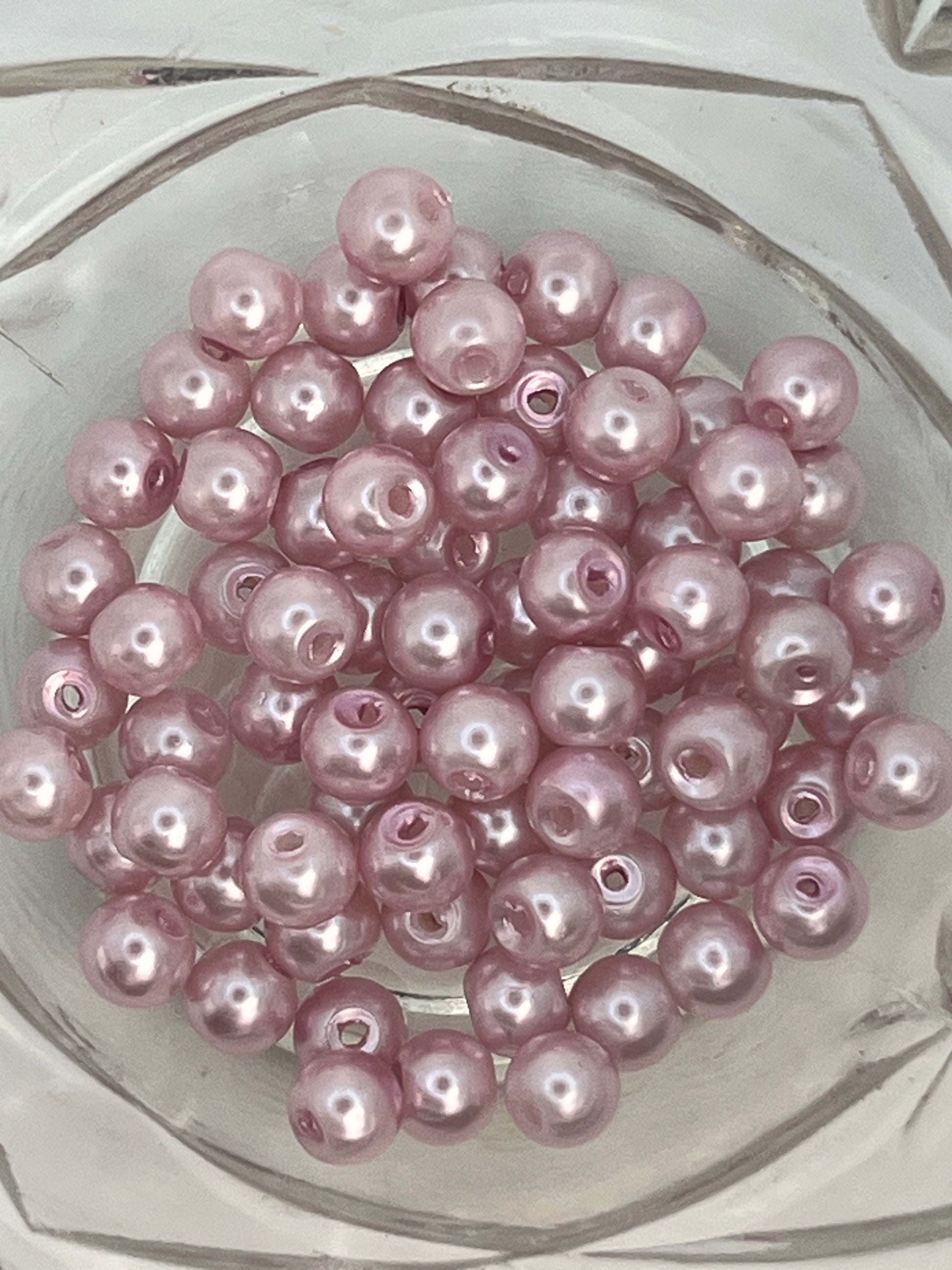 A cluster of 6mm flamingo pink glass pearl beads with a lustrous finish in a clear glass bowl.