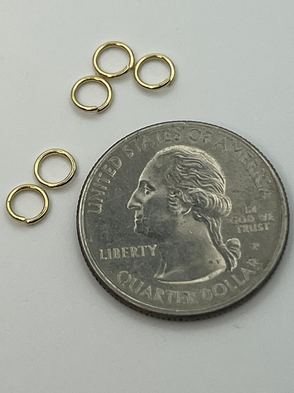 Golden 5mm 304 stainless steel jump rings next to a quarter.