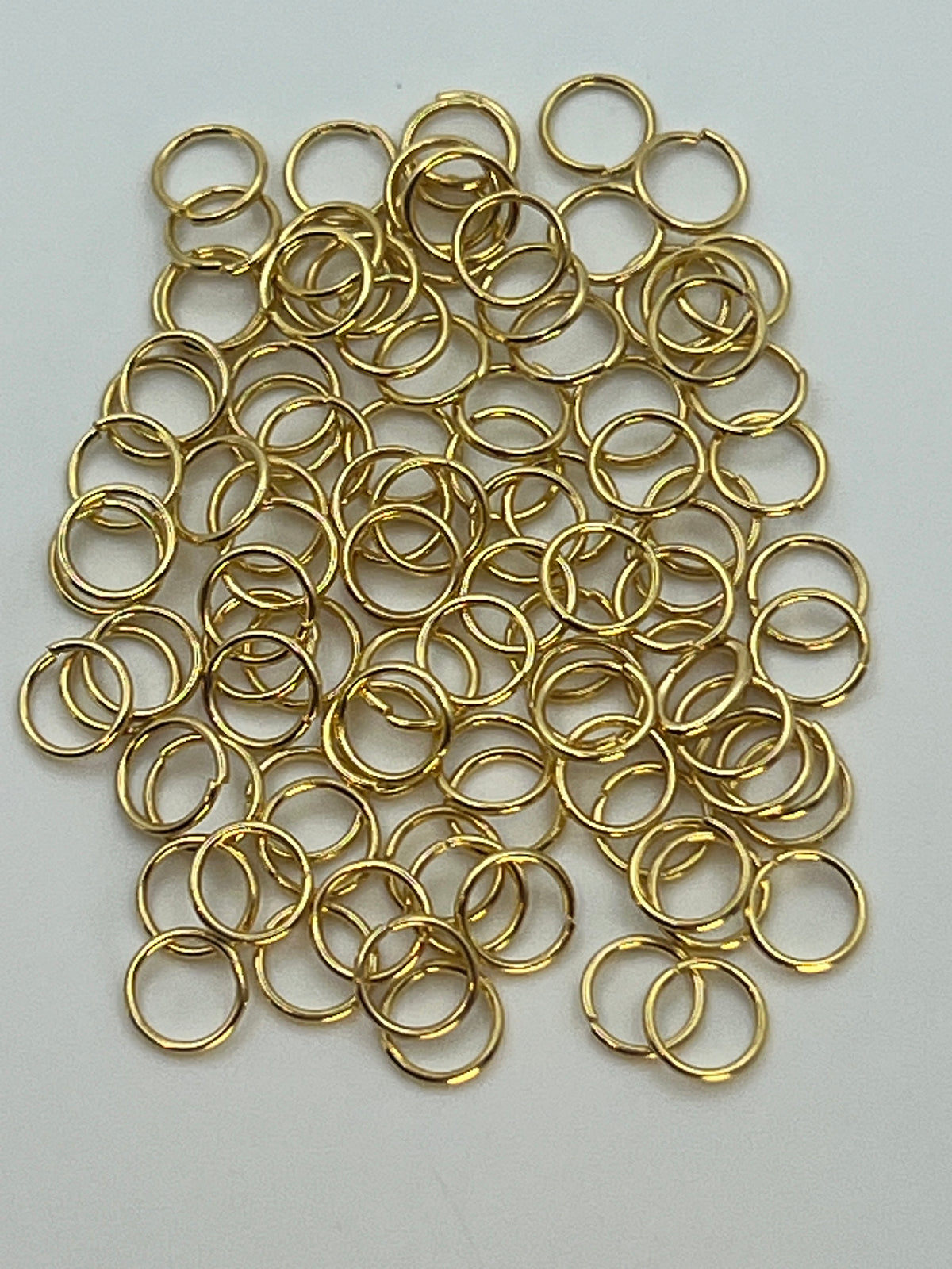 A pile of 6mm golden 304 stainless steel jump rings on a white background.