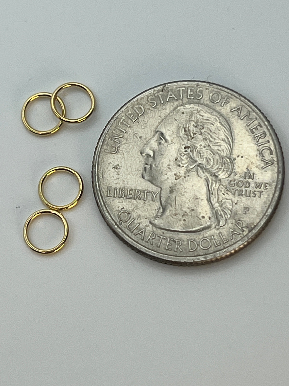 Four golden 6mm 304 stainless steel jump rings next to a US quarter for size comparison.