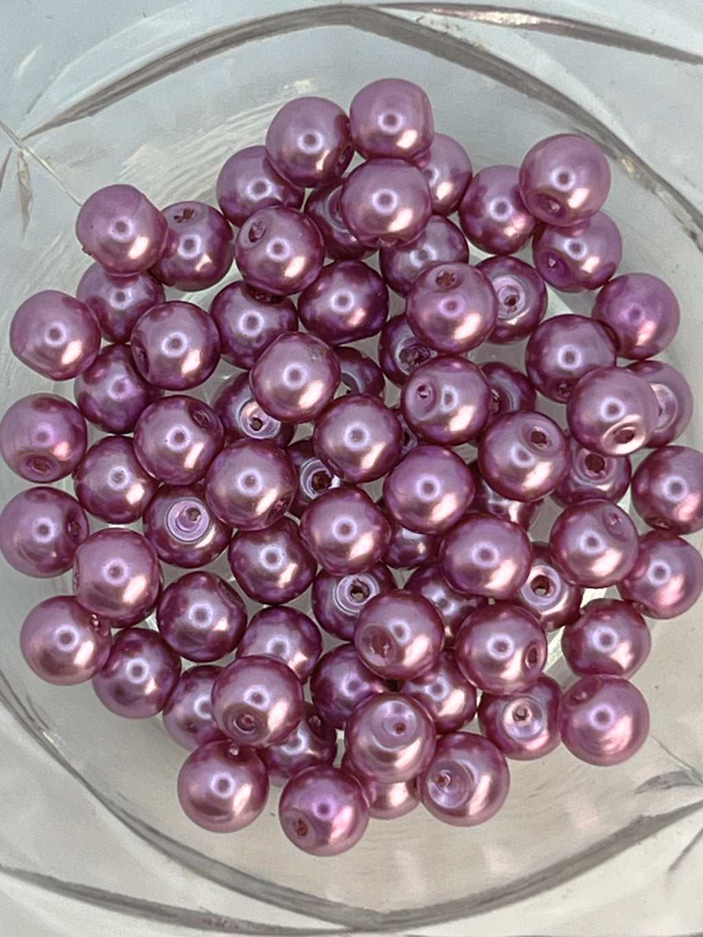 A cluster of 6mm medium orchid purple glass pearl beads in a clear glass bowl.