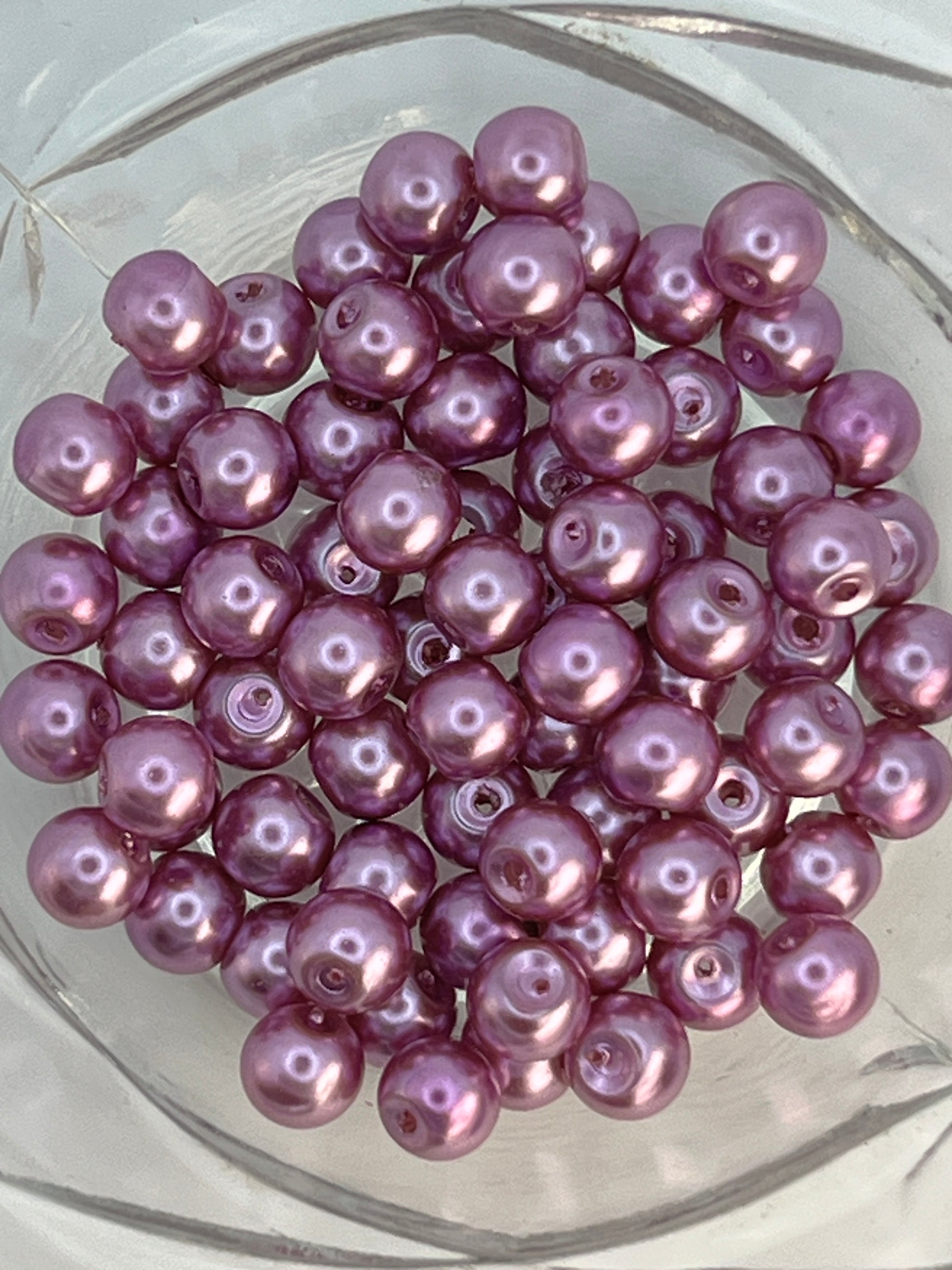 A cluster of 6mm medium orchid purple glass pearl beads in a clear glass bowl.