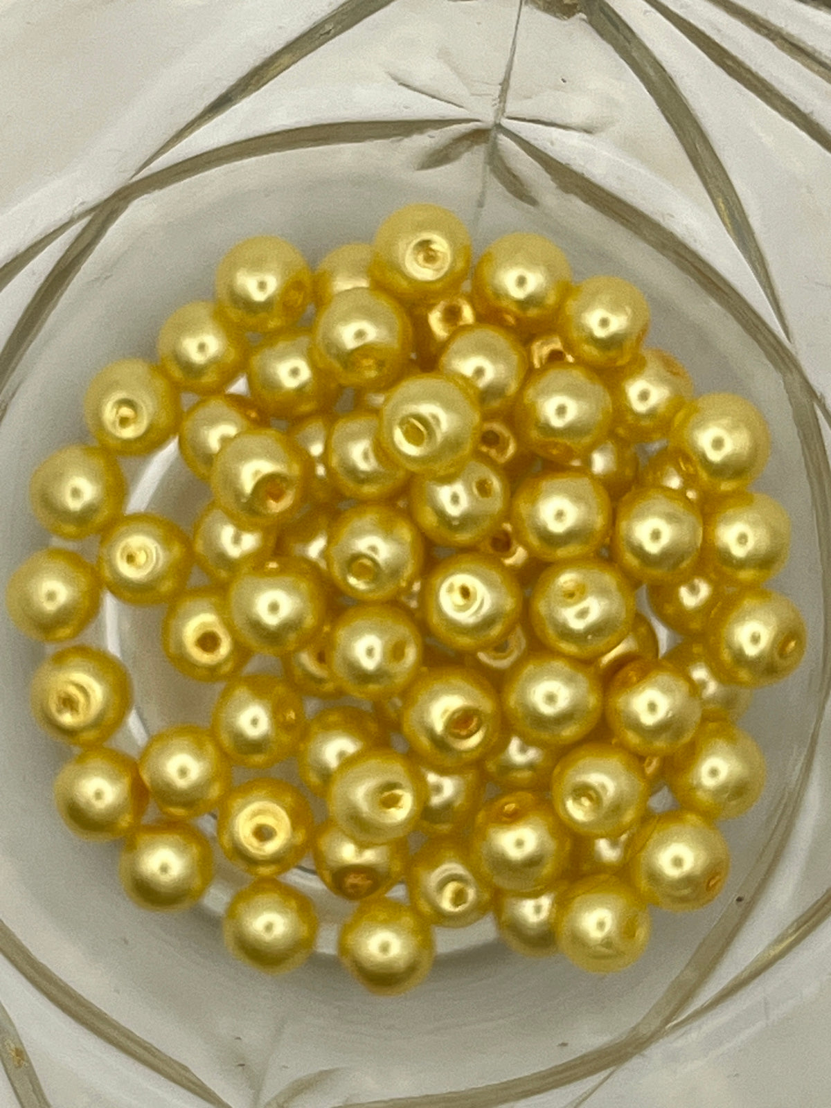 A collection of 6mm yellow glass pearl beads with 1mm holes for jewelry and craft making.