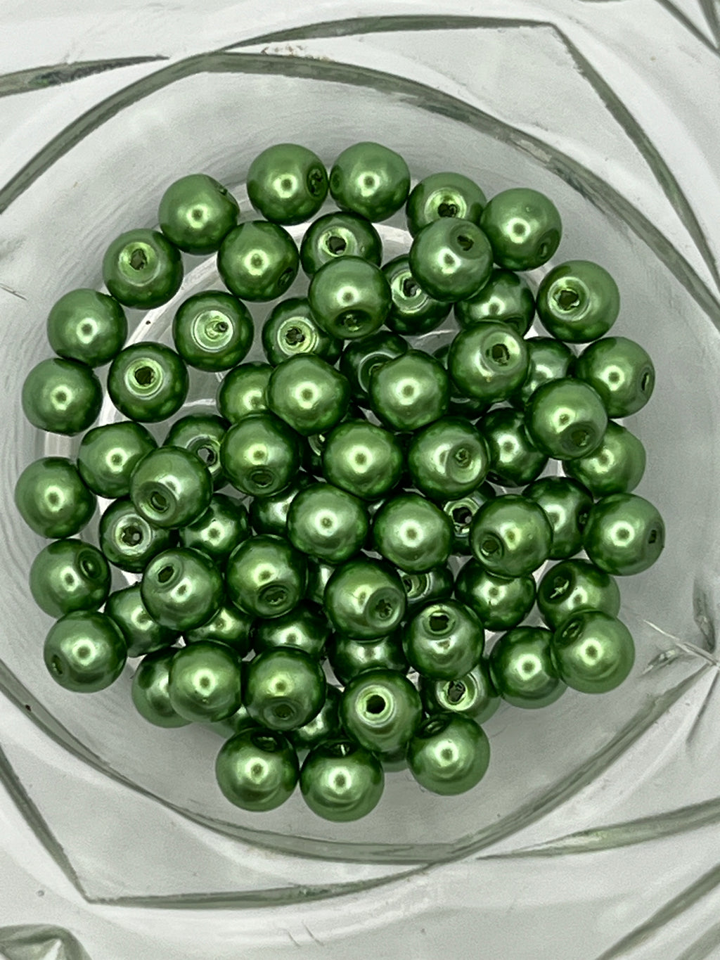 A collection of 6mm shiny green glass pearl beads with 1mm holes in a clear glass bowl.