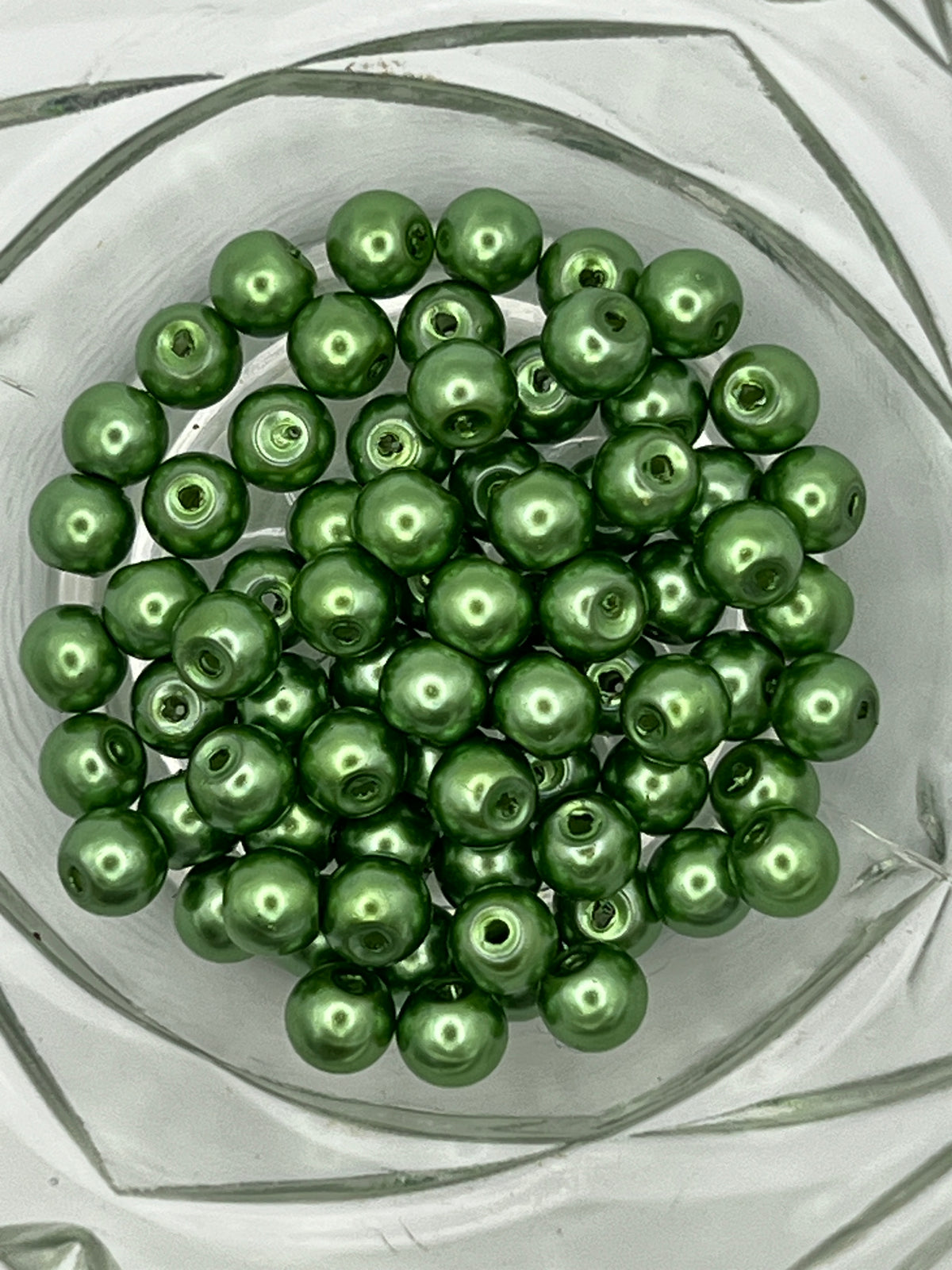 A collection of 6mm shiny green glass pearl beads with 1mm holes in a clear glass bowl.