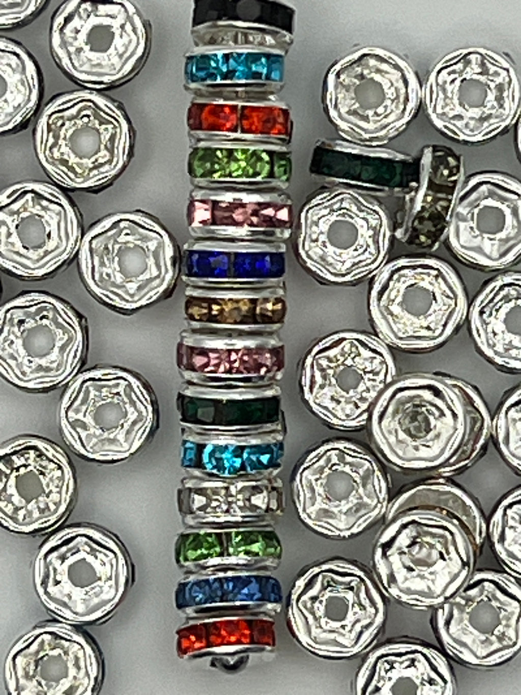 A stack of colorful rhinestone spacer beads next to silver spacer beads.