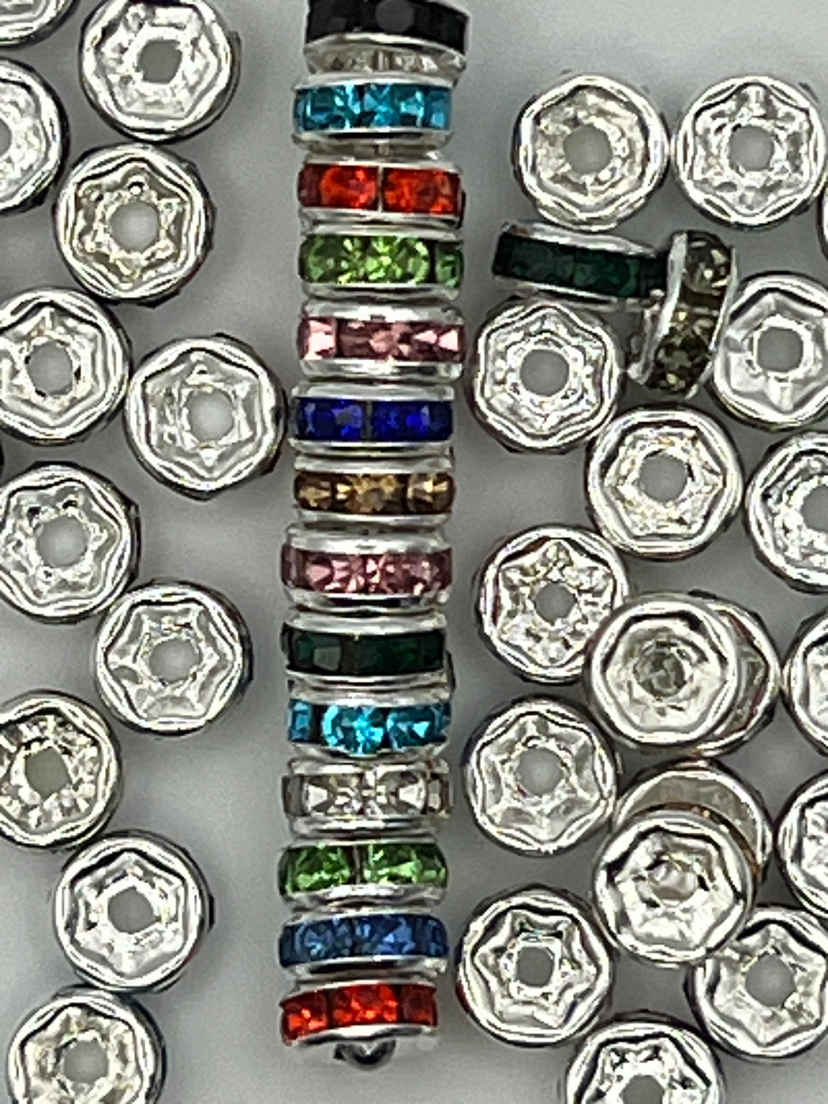 A stack of colorful rhinestone spacer beads next to silver spacer beads.