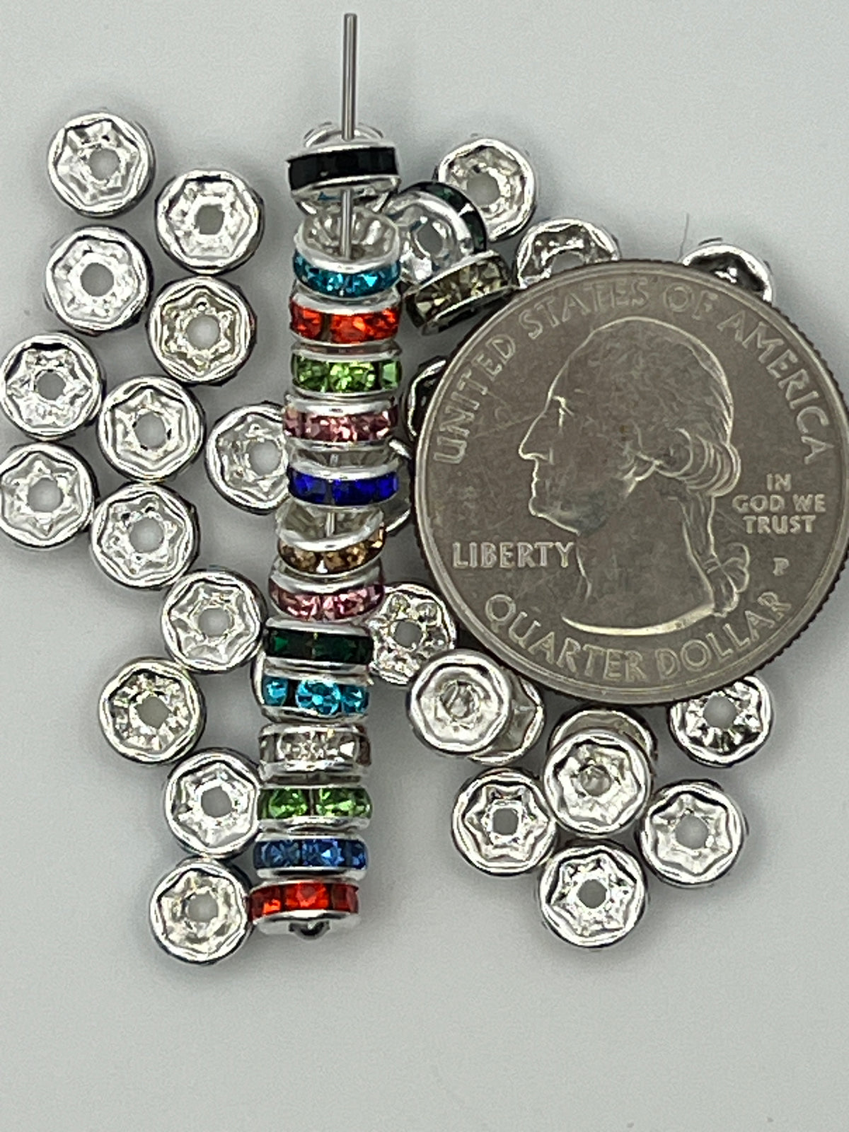 A stack of colorful rhinestone spacer beads next to a US quarter.