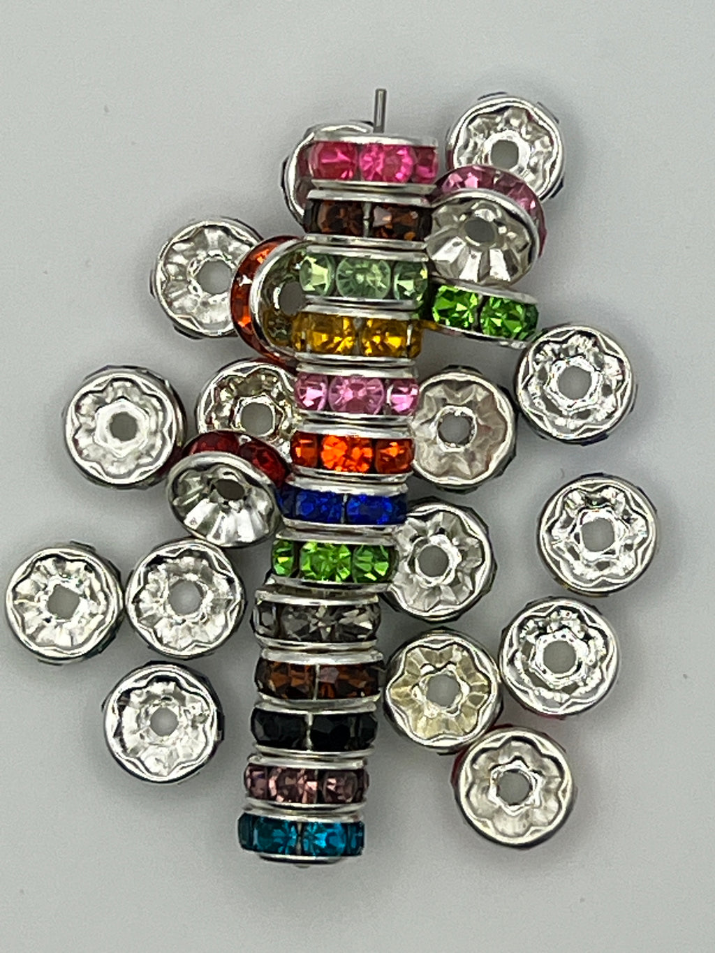 A stack and scattered assortment of 8mm silver-plated spacer beads with colorful glass rhinestones.