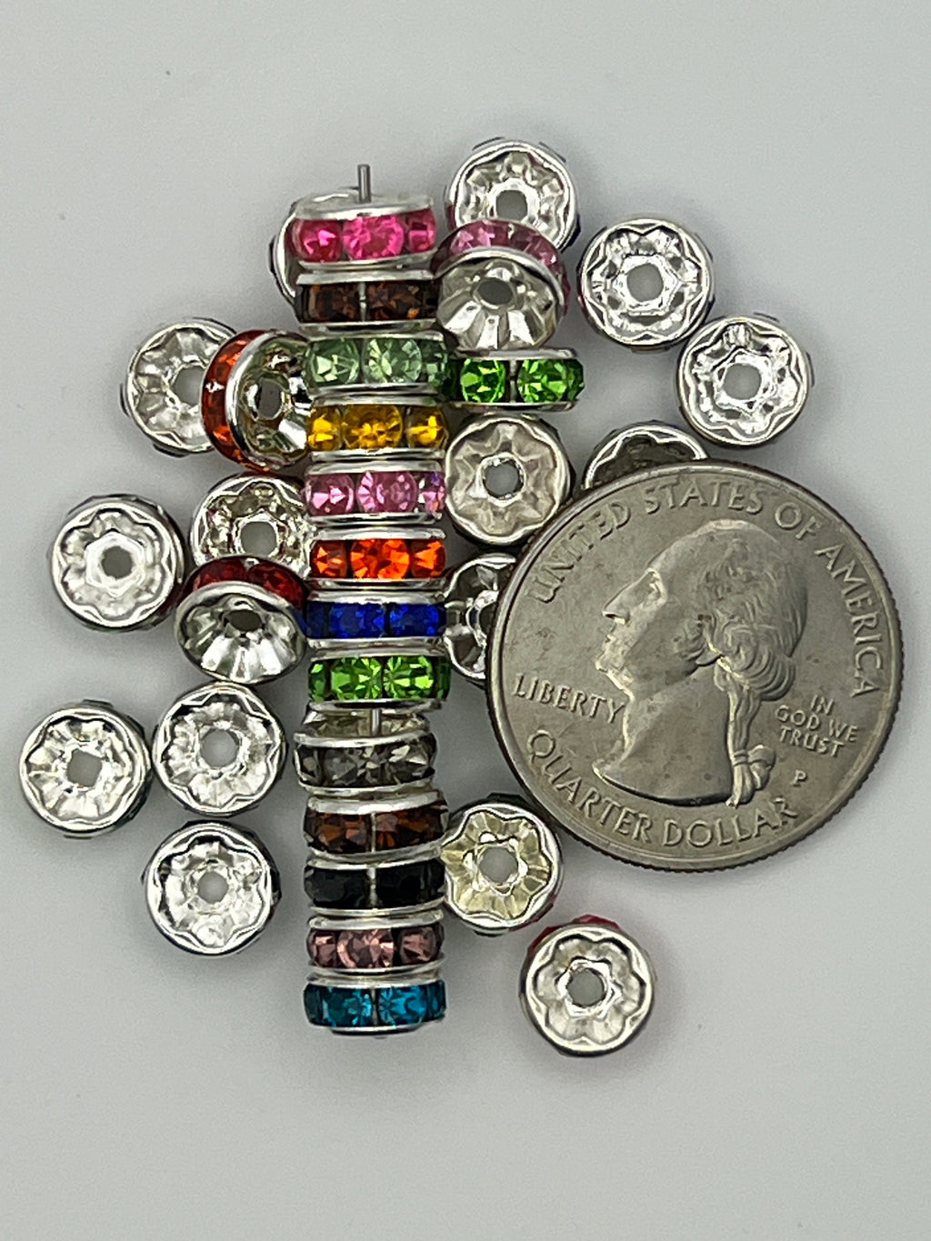 Assorted 8mm glass rhinestone spacer beads in various colors next to a US quarter for scale.