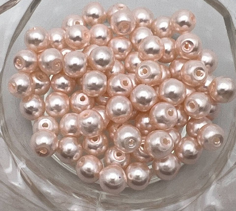 A pile of 6mm peach puff glass pearl beads with a 1mm hole.
