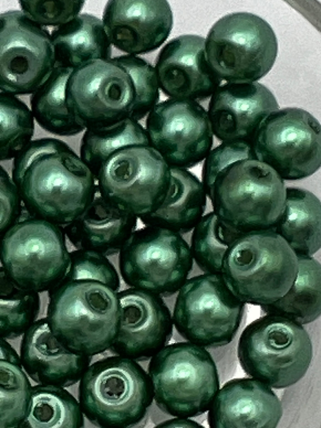 A pile of 6mm dark green glass pearl beads with visible holes.