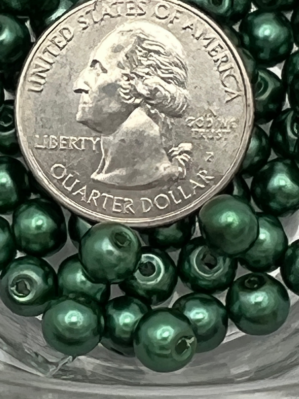 Dark green 6mm glass pearl beads with a quarter for scale.