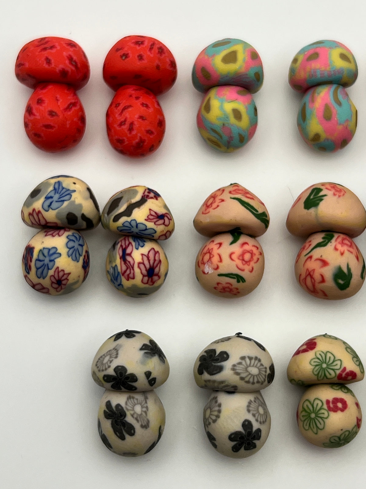 Assorted colorful polymer clay mushroom beads in floral and patterned designs for jewelry making.