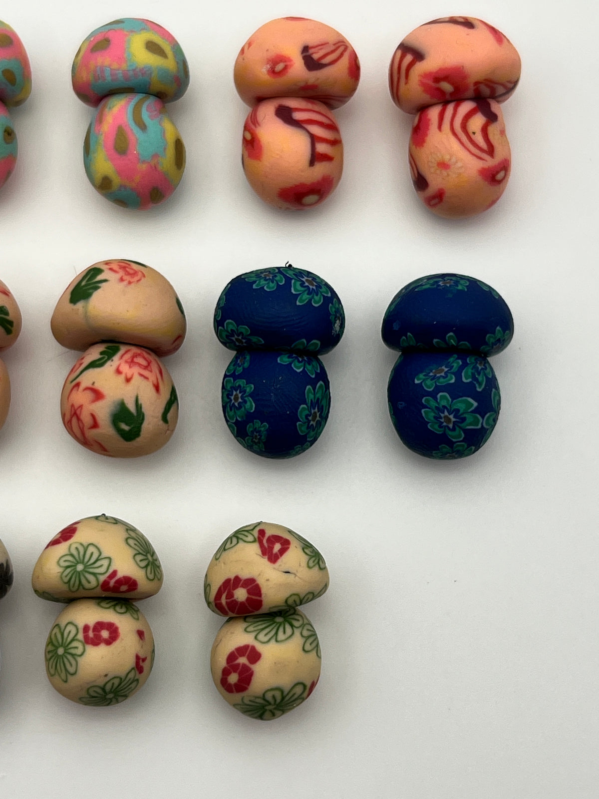 Assorted colorful polymer clay mushroom beads with floral and abstract patterns on a white surface.