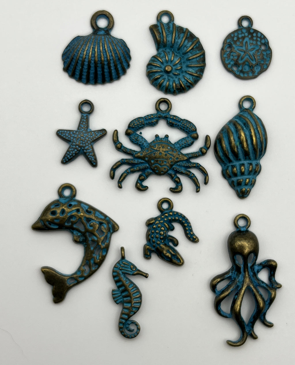 Ten antique bronze and blue patina Tibetan style ocean animal pendants on a white background.
