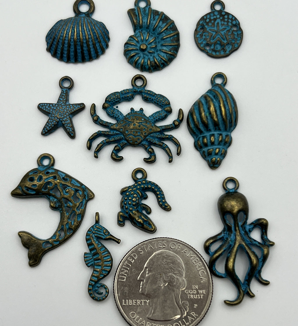 Ten antique bronze and blue patina ocean animal pendants next to a US quarter for scale.