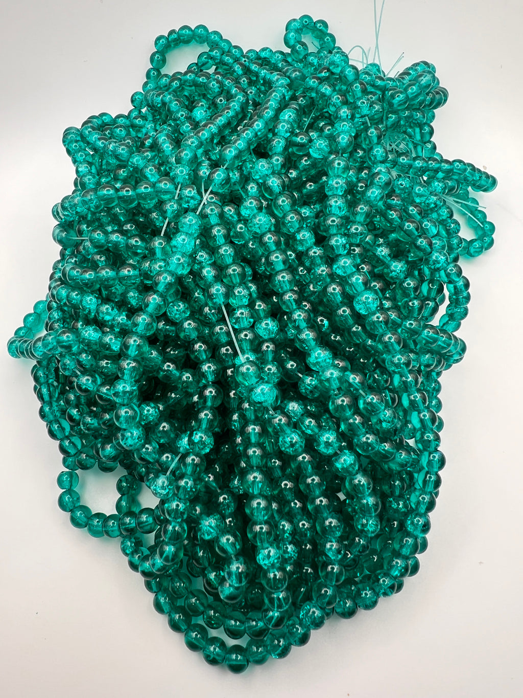Strands of 6mm teal crackle glass beads with internal fracturing on a white background.