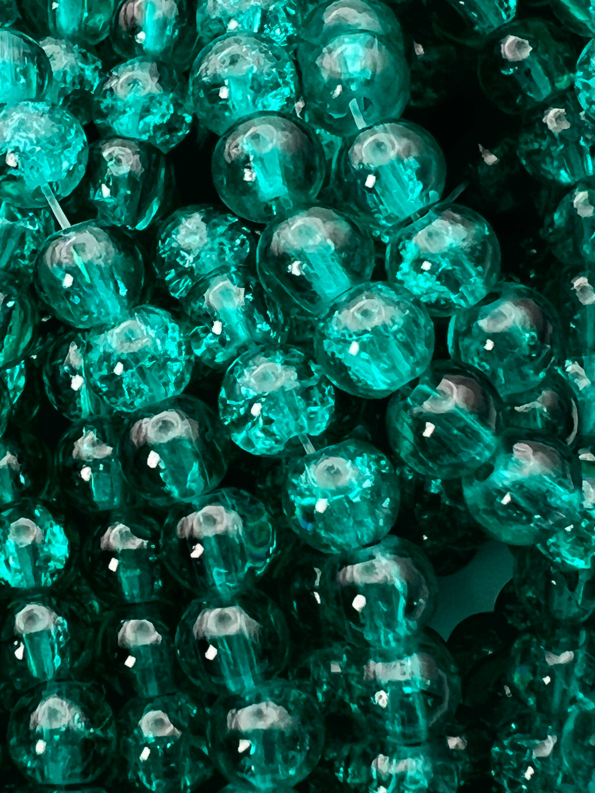 Close-up of 6mm teal crackle glass beads with intricate internal fracturing and a glossy finish.