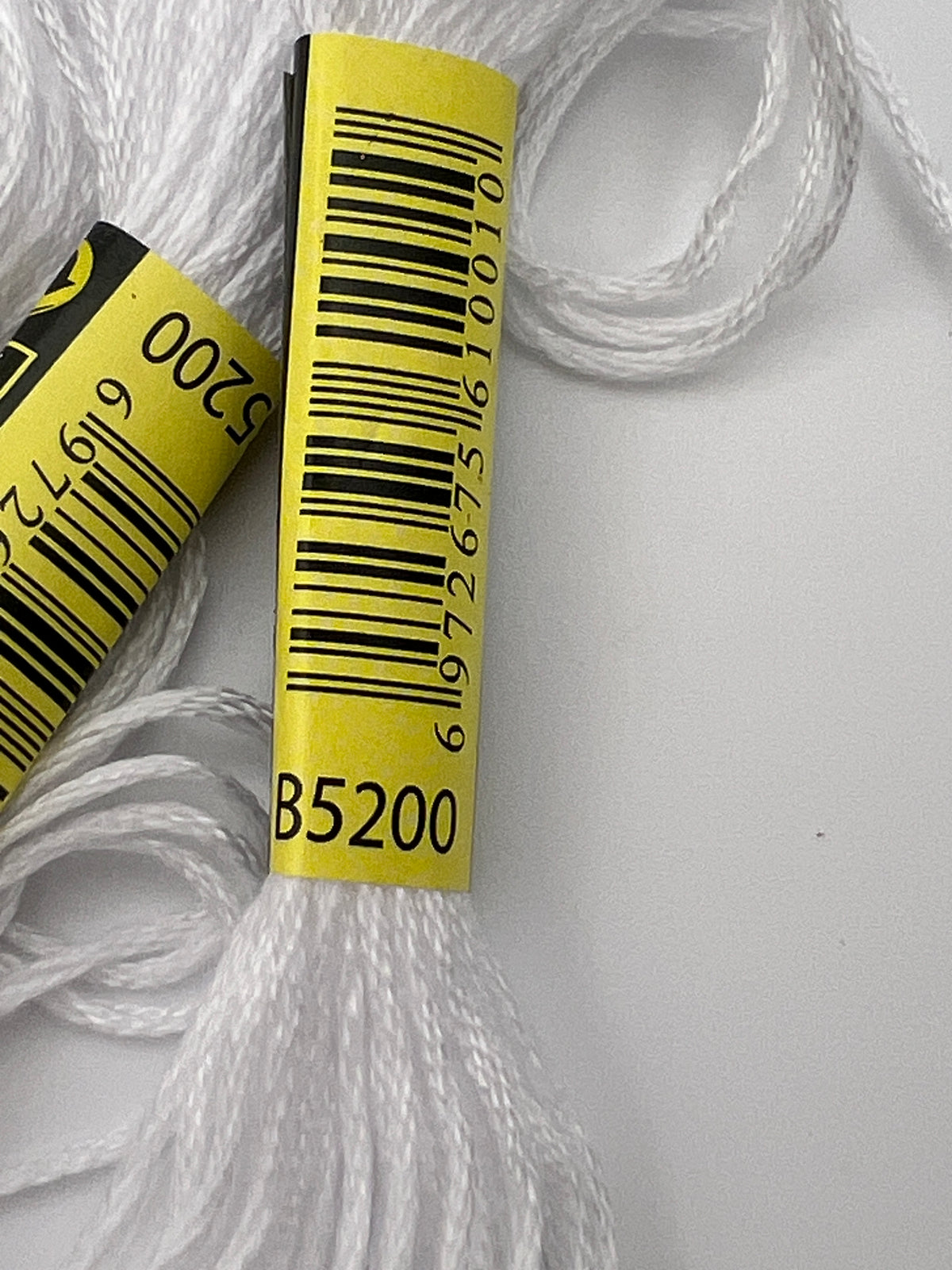 Close-up of white 6-ply embroidery thread skeins with yellow labels showing code B5200.