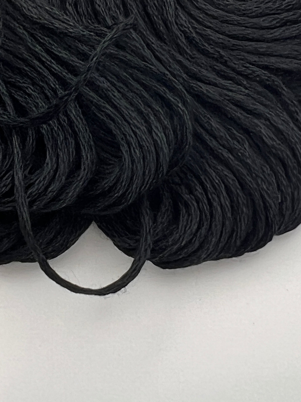 Close-up of a bundle of 1.4mm black embroidery thread skeins on a white background.