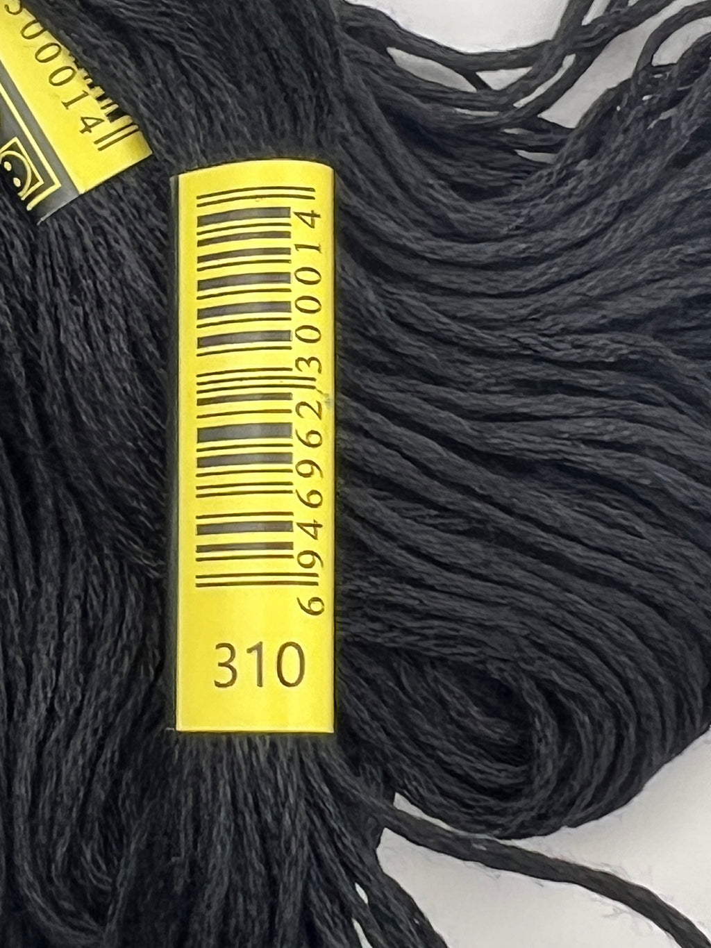 Close-up of black 1.4mm embroidery thread skein with yellow label showing color code 310.