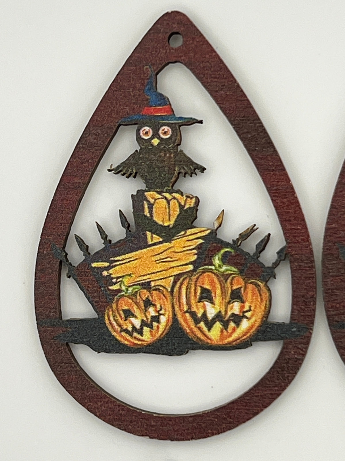Teardrop-shaped wood pendant with a printed owl in a witch hat perched above two jack-o'-lanterns.