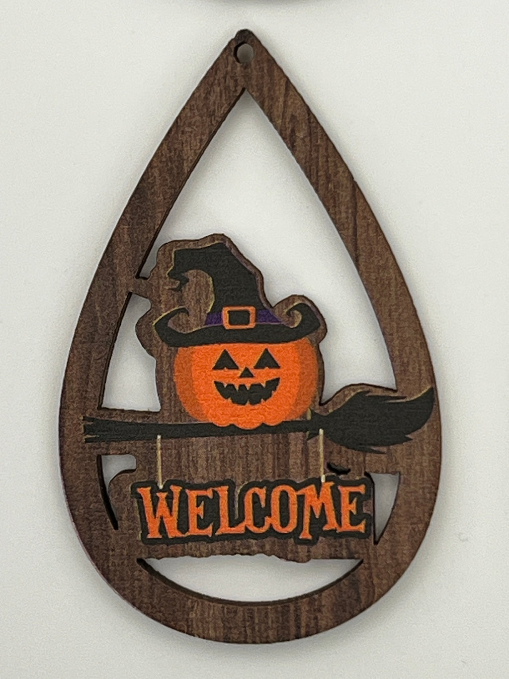 Teardrop-shaped wood pendant with a printed jack-o'-lantern in a witch hat and a Welcome sign.