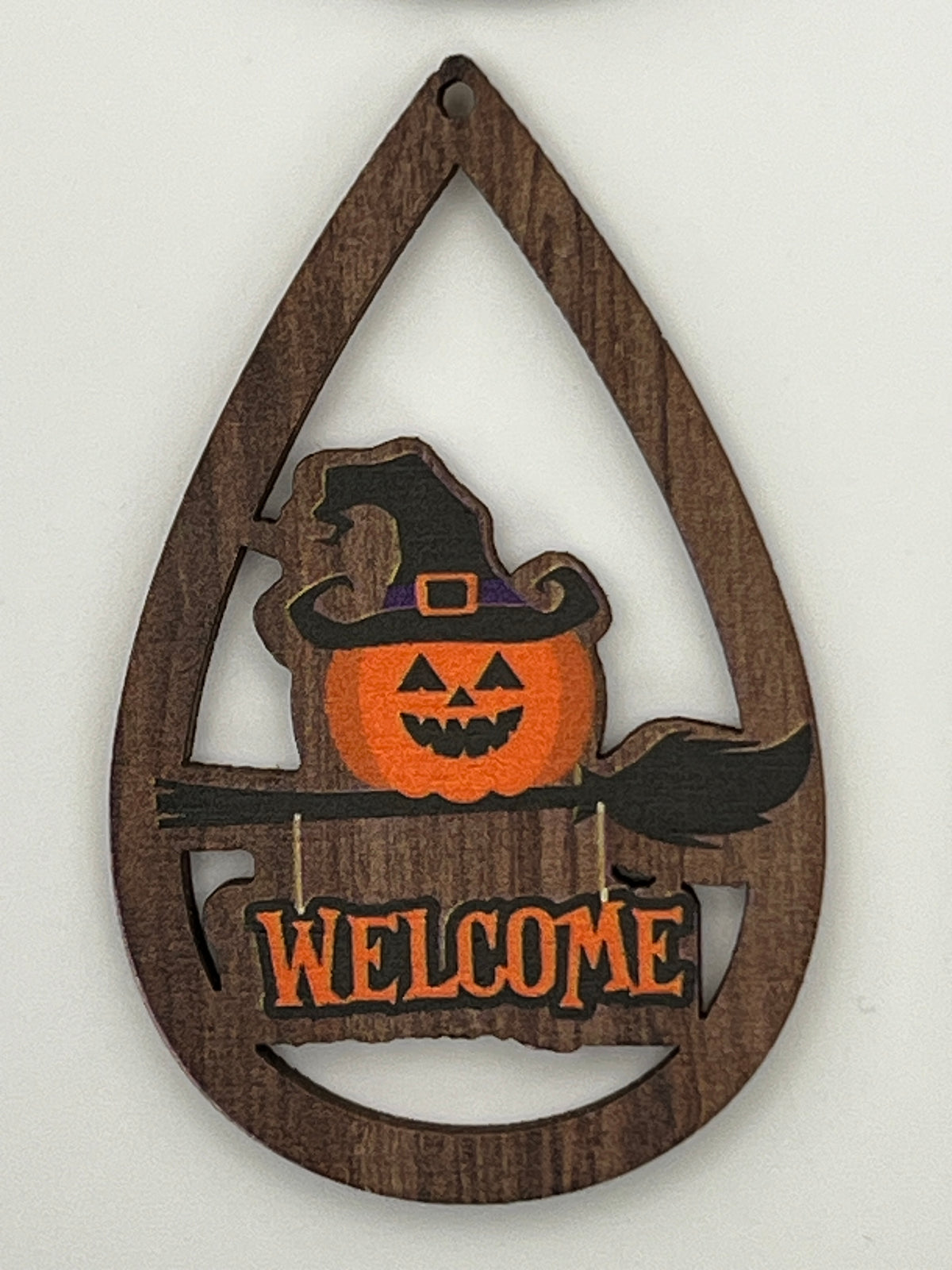 Teardrop-shaped wood pendant with a printed jack-o'-lantern in a witch hat and a Welcome sign.