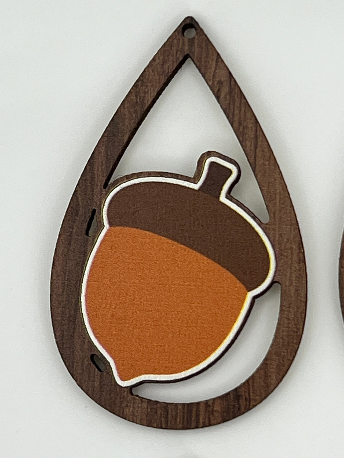 Teardrop-shaped dark wood pendant featuring a printed acorn design in brown and orange.