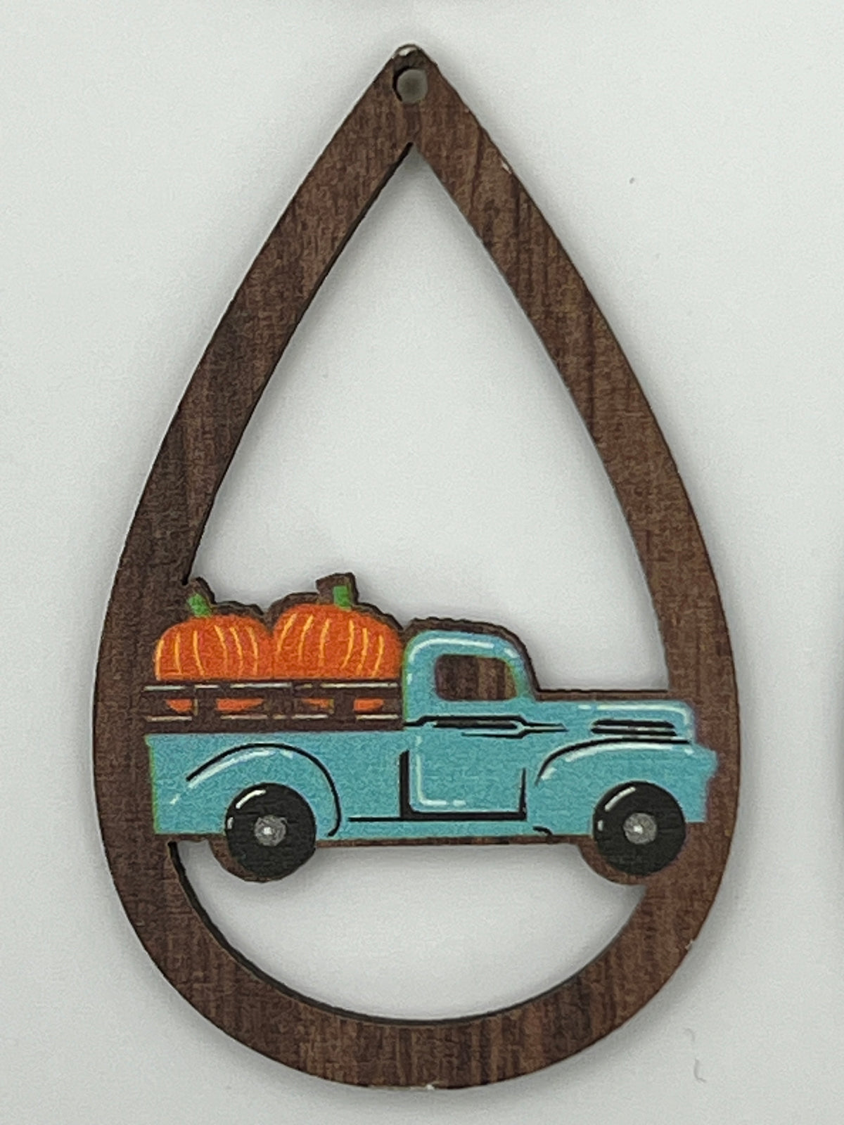 Teardrop-shaped wood pendant with a cut-out center featuring a blue truck carrying orange pumpkins.