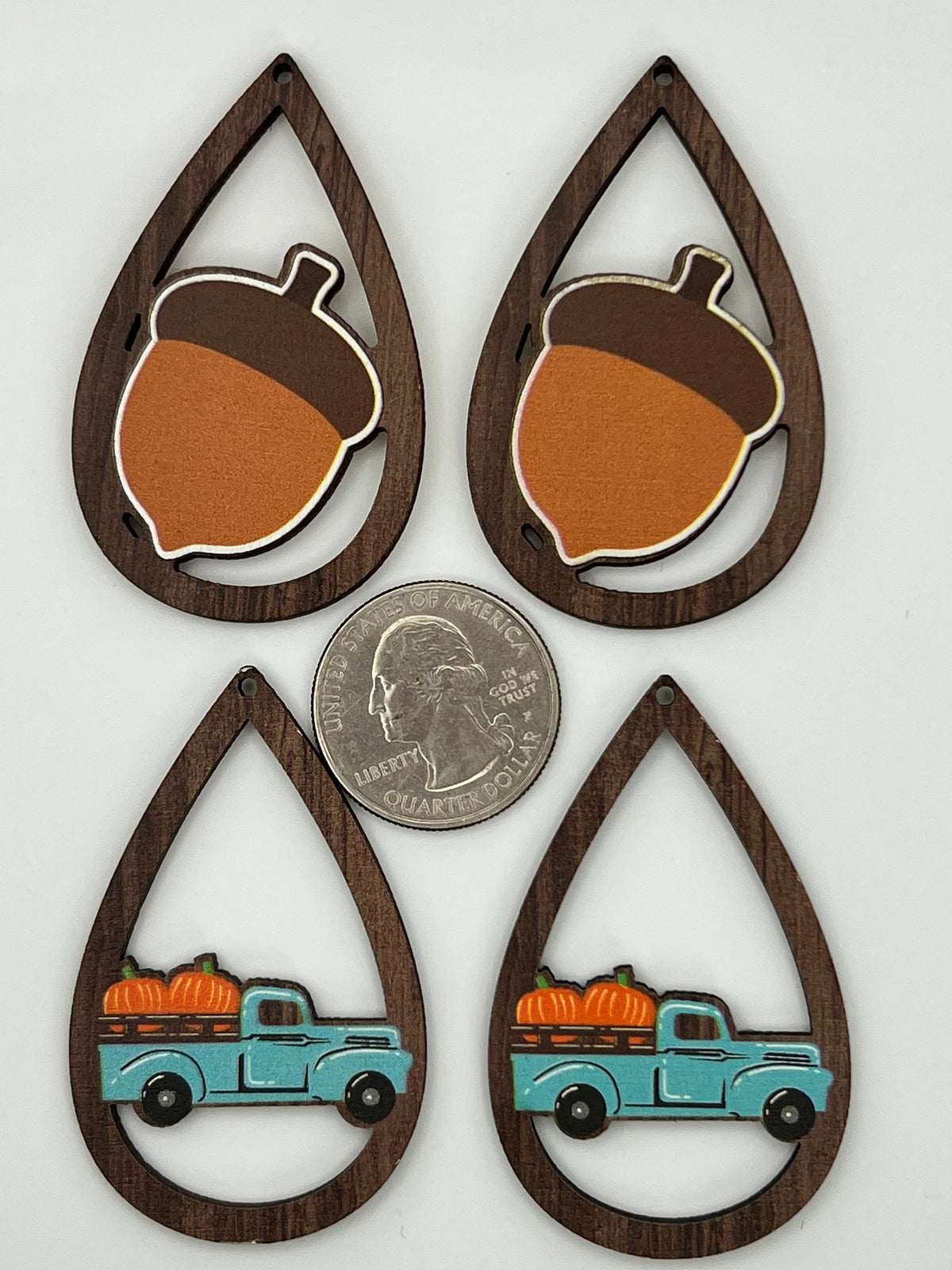 Four teardrop-shaped wood pendants with acorn and blue truck designs next to a US quarter.