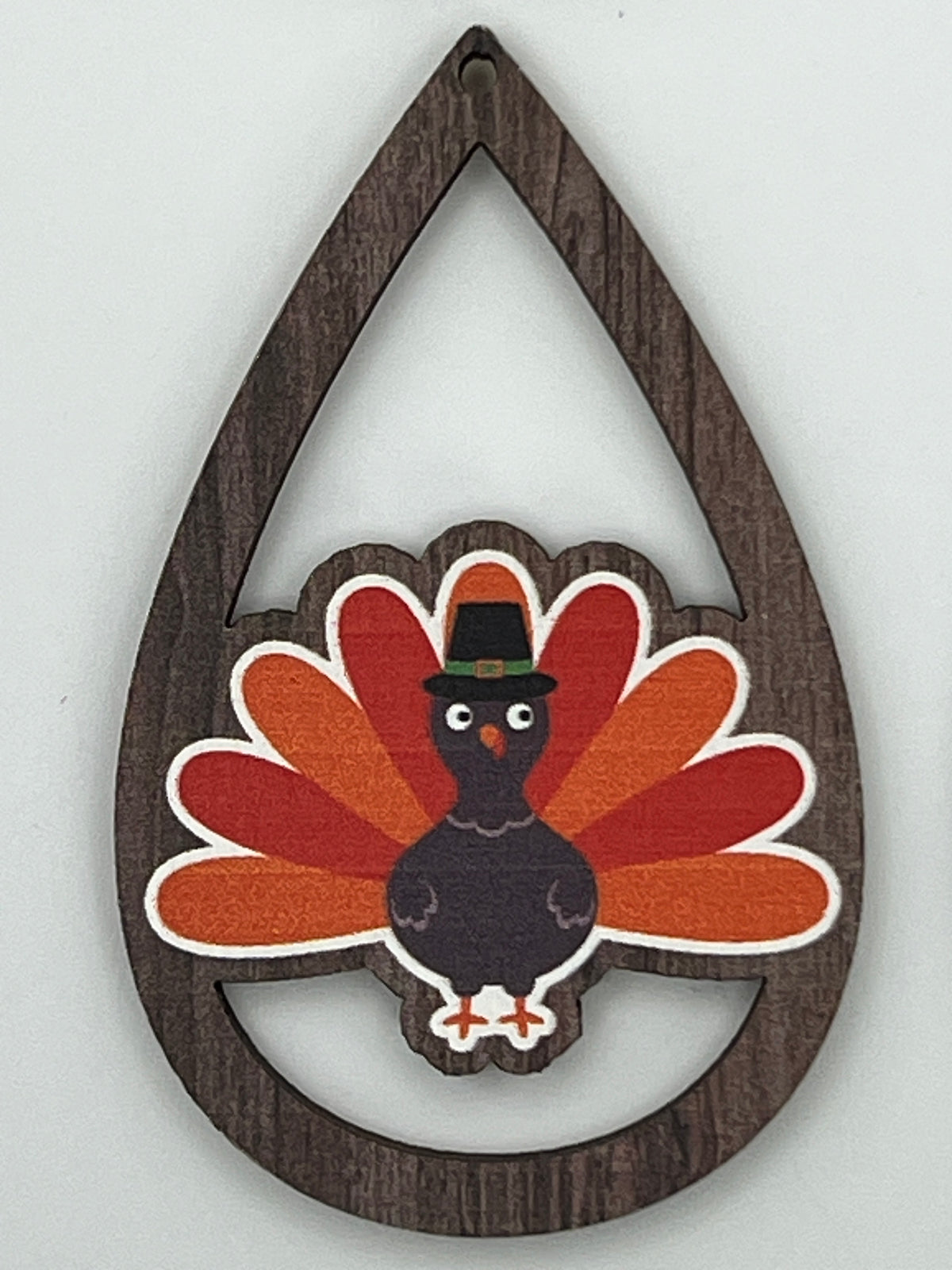 Teardrop-shaped dark wood pendant featuring a colorful cartoon turkey with a pilgrim hat.