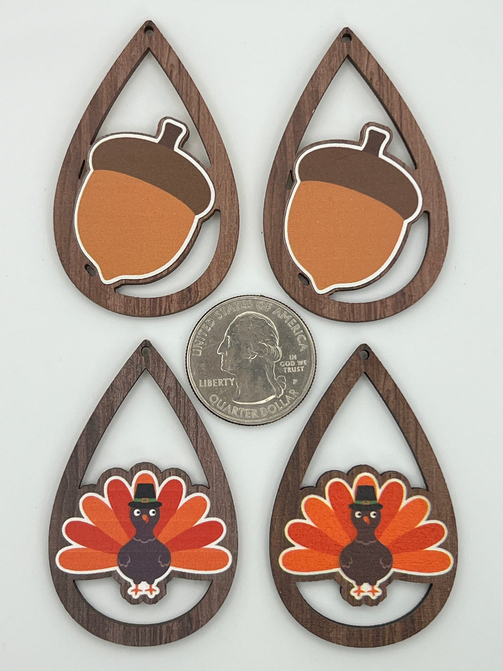 Four teardrop-shaped wood pendants with acorn and turkey prints next to a quarter for scale.