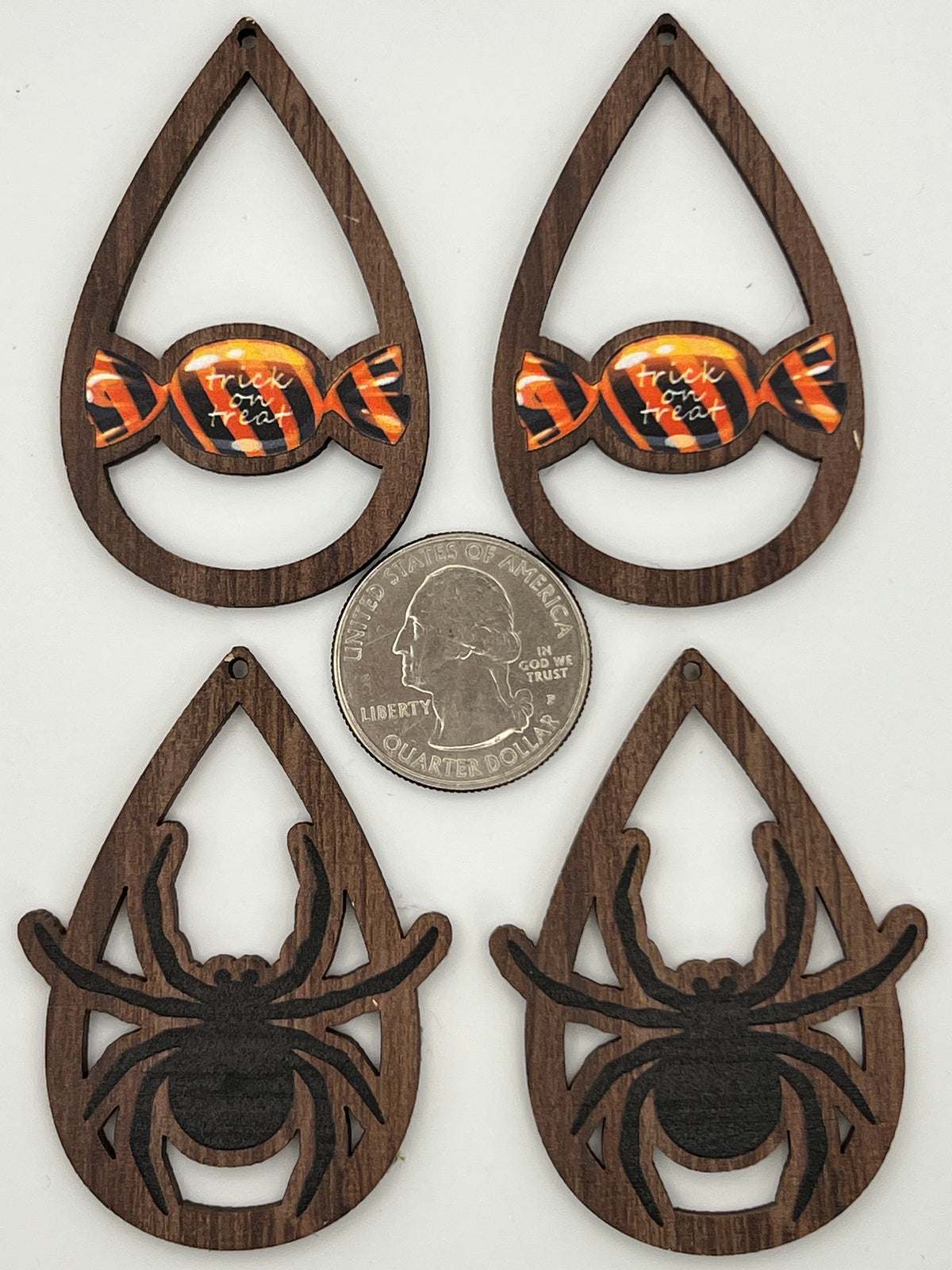 Four wooden teardrop pendants with spider and candy designs next to a quarter for scale.